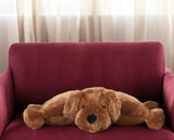 Brown plush dog pillow resting on red couch in a sunlit room