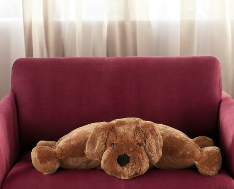 Brown plush dog pillow resting on red couch in a sunlit room