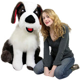 Child sitting beside large Saint Bernard plush toy smiling for photo