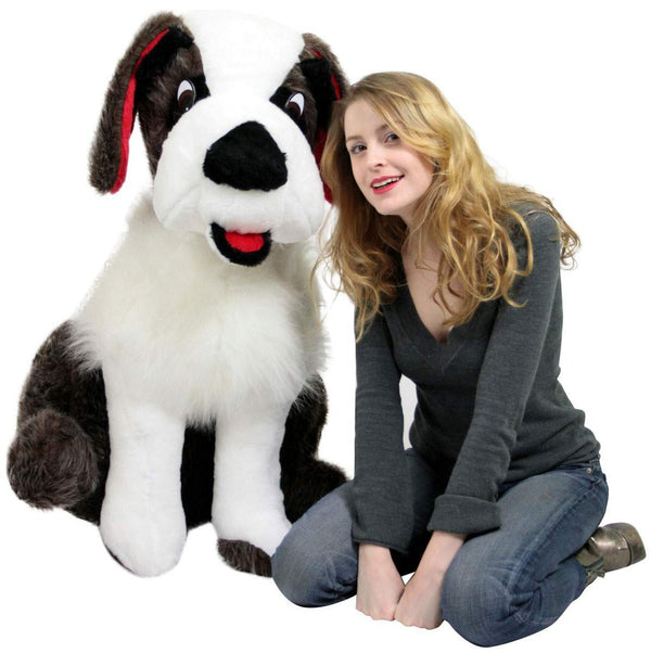 Child sitting beside large Saint Bernard plush toy smiling for photo